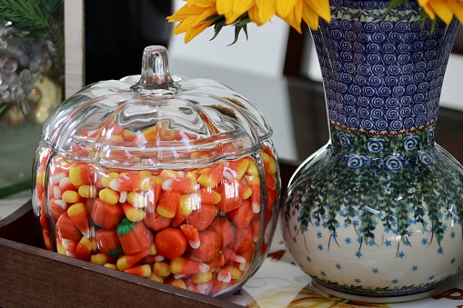 A pumpkin shaped, glass cookie jar that is filled with candy corn.