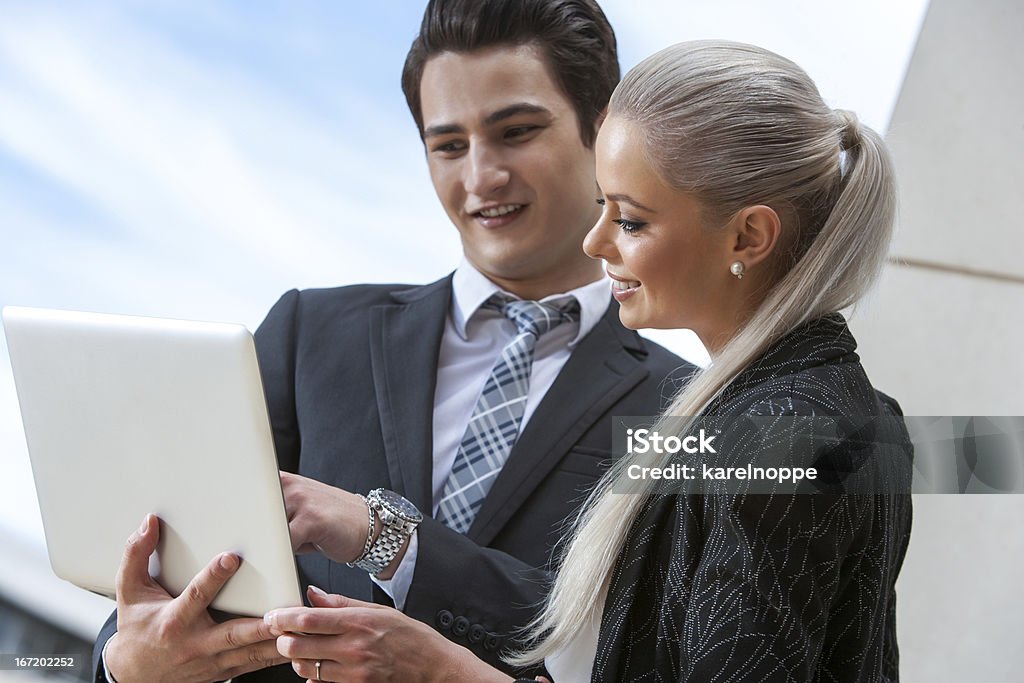 Business partners reviewing information on laptop. Portrait of young business partners reviewing information on laptop outdoors. Adult Stock Photo