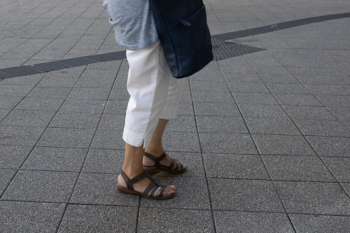 Woman in her mid-50s wearing sandals stands on the street
