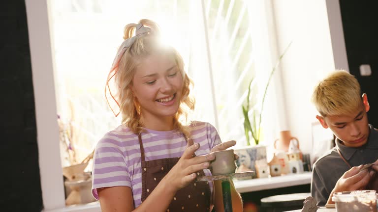 Cute blonde girl makes clay cup using manual potter wheel