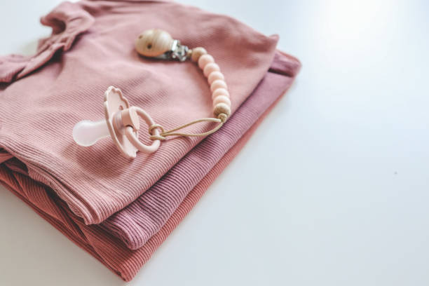 istock Stack of pink baby clothes and baby pacifier on white background 1672103124