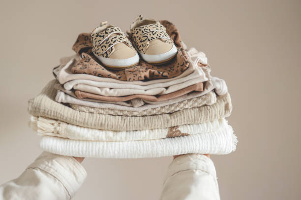 istock Stack of baby clothes in hand on neutral background 1672104701