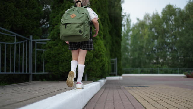 Little Schoolgirl Walking On Curb, Keeping Balance, Back View, Closeup Of Legs Of Little Child Girl