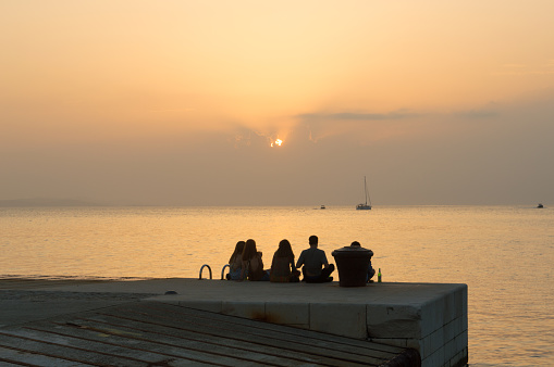 Zadar, Croatia - 21 July 2023: Young friends enjoying amazing sunset on the pier during the hot summer day