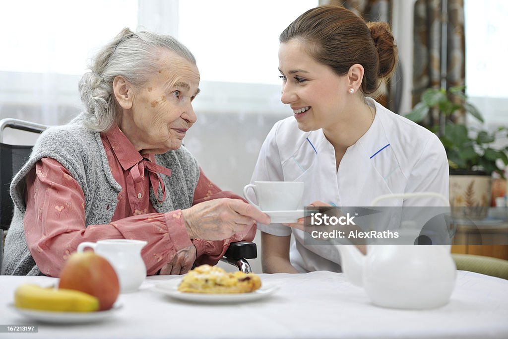 Carer in nursing home handing an elderly woman a cup of tea Senior woman eats lunch at retirement home Eating Stock Photo