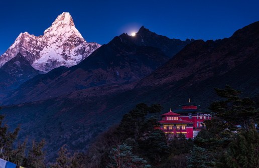 Ama Dablam illuminated by alpenglow and moonlight overlooking Tengboche Monastery and Buddhist prayer flags deep in the Himalayan mountains of Nepal.