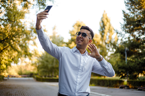 A young manager in a white shirt is making a selfie in the park