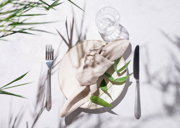 istock Festive table setting with plate and glass for a celebration with eucalyptus branches on a light background with shadows. Restaurant menu concept. 1672183678