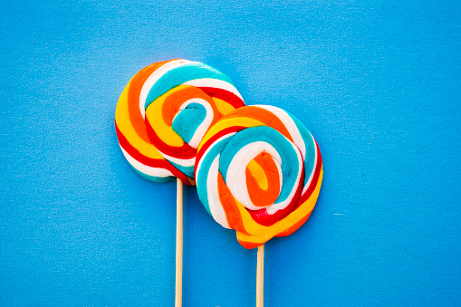 Colorful lollipop on a blue background. Red, white , orange and blue stripes on a candy. Minimal concept. Candy shop series.