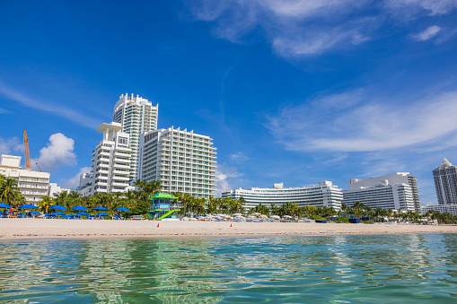 Miami Beach. USA. 09.10.2023.  Beautiful view of white sandy beach Atlantic Ocean with sun loungers, sun umbrellas on backdrop of buildings.