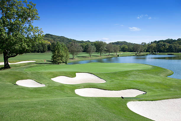 Sand traps and water hazard on pristine golf course A putting green across from a large water hazard with multiple sand traps surrounding it. country club stock pictures, royalty-free photos & images