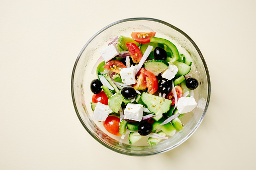 Greek salad in glass bowl on yellow background.