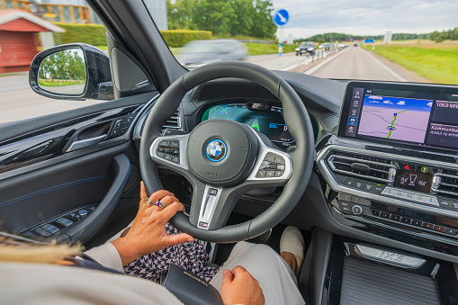 Sweden. Uppsala. 31.08.2023. Close-up view of woman driver driving new  BMW iX3 M Sport black car electric model on highway.