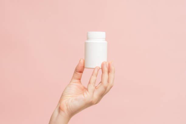 istock White bottle (plastic tube) in hand on pink background. Packaging for vitamins, pill or capsule, or supplement. Mockup for product branding 1672271056