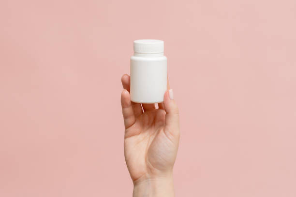 istock Plastic bottle (tube) in hand on pink background. Packaging for vitamins, tablets or capsule, or supplement 1672271157
