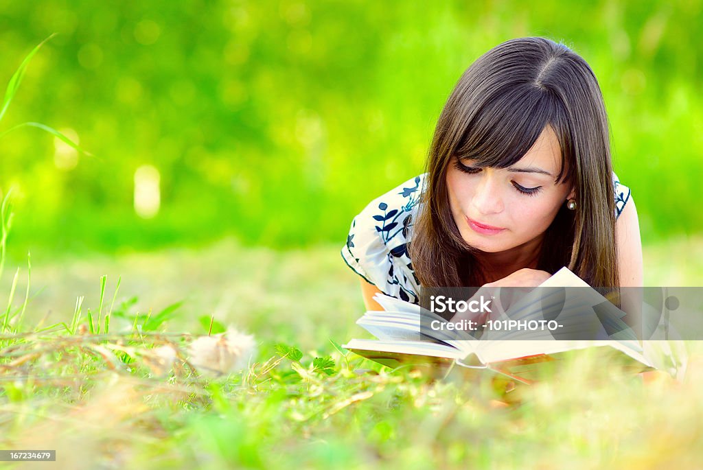 Girl reads book on meadow Young beautiful woman lays on green field and reads book. Adult Stock Photo