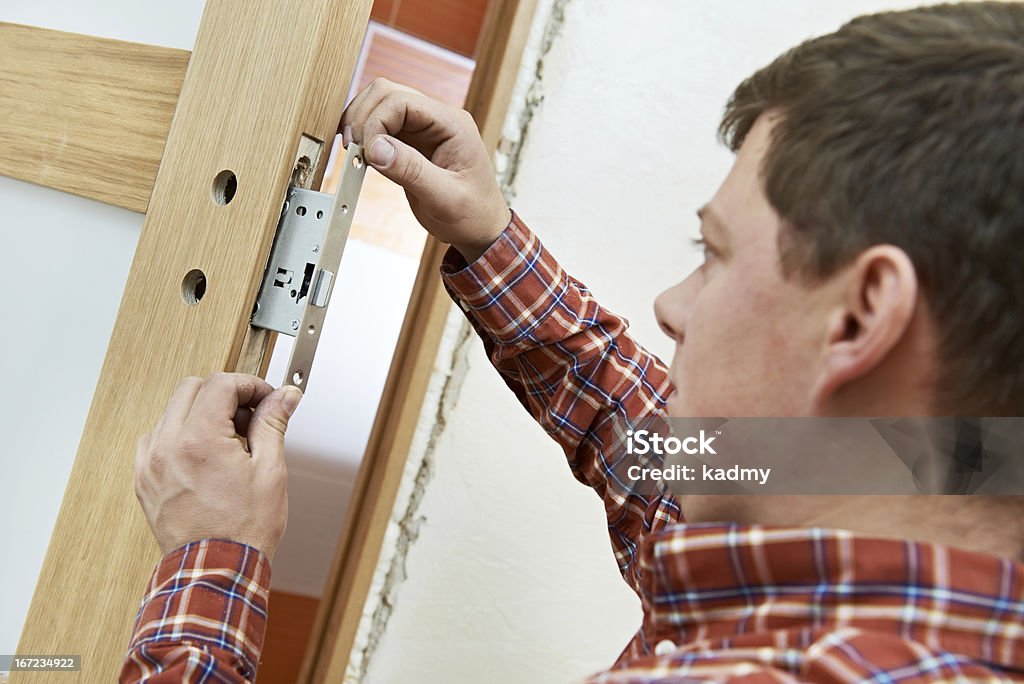 carpenter at door lock installation Male handyman carpenter at interior wood door lock installation Adult Stock Photo