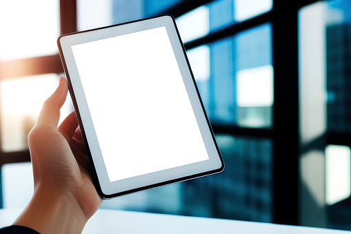 Male hand holding tablet with white blank screen in modern office.