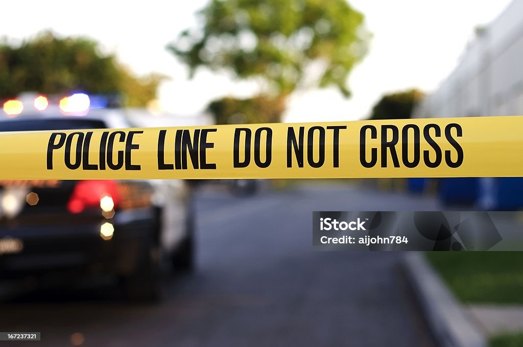 A police crime scene tape close-up A blurred police car in the background behind yellow crime scene tape.  Barricade Tape Stock Photo