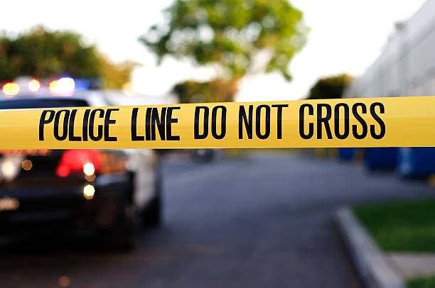 A police crime scene tape close-up A blurred police car in the background behind yellow crime scene tape.  police tape stock pictures, royalty-free photos & images