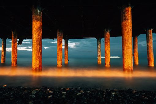 Professional high quality photo. iron columns at the seashore. Photo of waves on a long exposure. Evening photo of the sea and columns with rust.