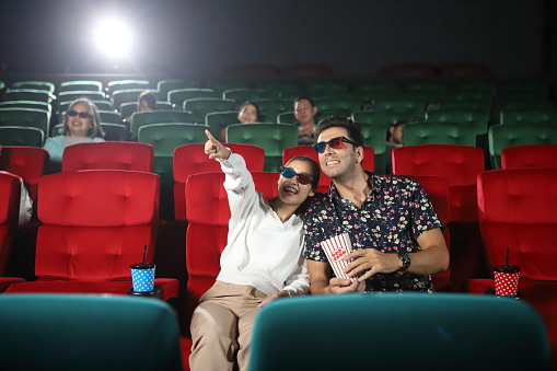 Happy people in cinema enjoying a movie, popcorns and beverages over the weekend.