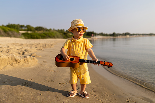 Portrait of cute baby boy playing guitar on the beach. Summer music concept.