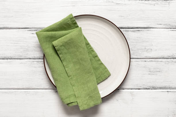 istock White plate with green napkin on a white wooden table. Top view, flat lay, copy space. 1672422648
