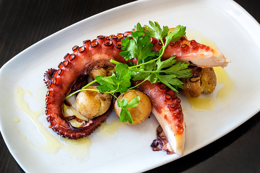 Boiled octopus tentacles according to a Mediterranean recipe with potatoes and parsley. High quality photo
