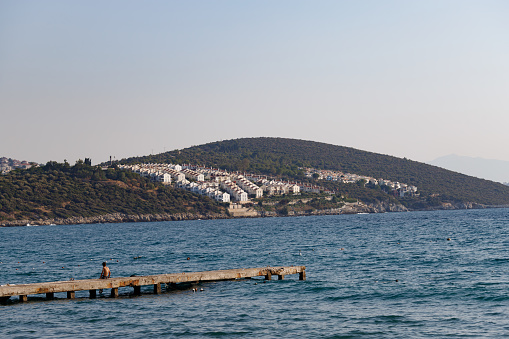 View of a settlement in Kusadasi from the sea, Turkey with a jetty with a boy looking at the sea.