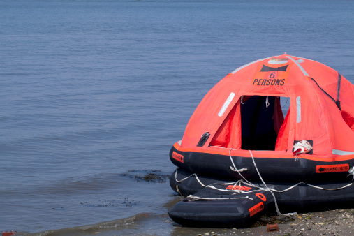 An inflatable 6 person life-raft stranded on a beach. Off center for copy space