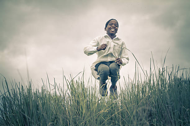 A happy smiling young South African boy (from the Xhosa tribe) jumping and laughing in a field of tall grass.