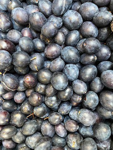 Stock photo showing close-up, elevated view of a pile of ripe Damson plums (Prunus domestica subsp. insititia) being sold from a produce display at a fruit and vegetable outdoor market.