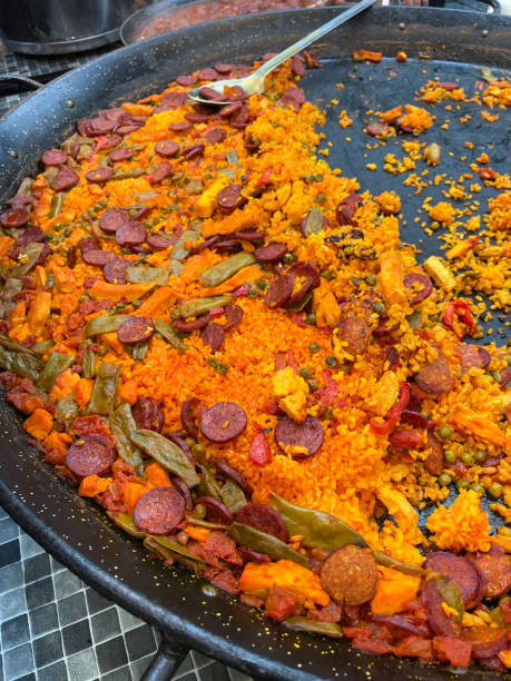 Stock photo showing close-up, elevated view of Spanish chicken and chorizo paella cooking on kitchen hob almost ready eat. This paella has short grain white rice, saffron, chorizo slices, diced chicken, flat green beans, red peppers served in pan for dinner.