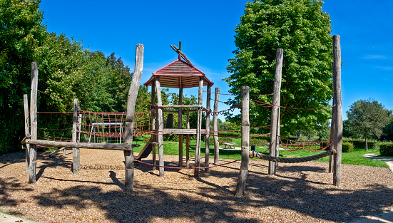 Climbing castle made of wood on a deserted public playground in summer with nice weather and cloudless sky, bordered by deciduous trees
