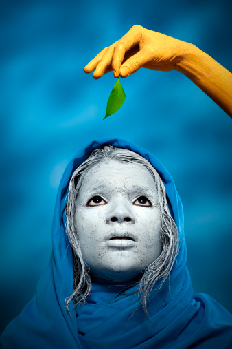 In this conceptual image a women wearing blue shawl looking hopefully upward towards a last green leaf which is in yellow, orange painted hand.