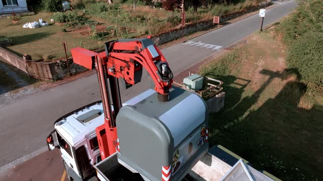 Refuse truck is collecting recycled glass from containers by the roadside, lifting up and unloading them in the back of the truck, glass recycling concept.