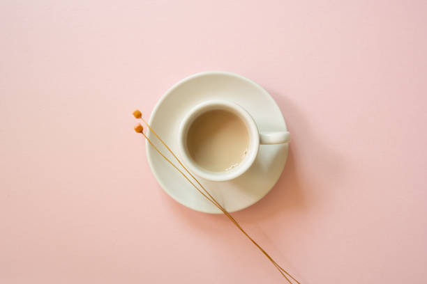 White cup of coffee with dry flower on pink background. top view stock photo