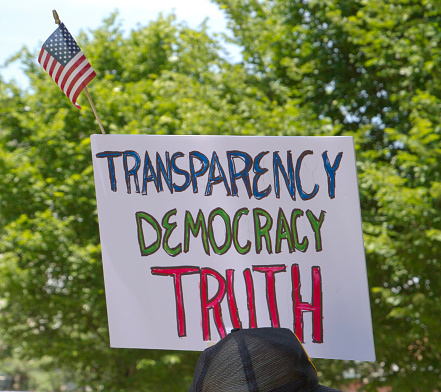 Close up of an American flag and political sign at a political rally saying Transparency, Democracy, Truth