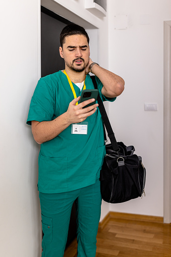 Tired handsome mid adult Caucasian man using mobile phone in hallway of his apartment just came home from work