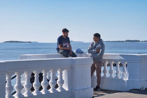 colonia del sacramento, uruguay - november 1 2022: young men sitting on the elagant stone edge of the boardwalk with view over the Rio de la Plata