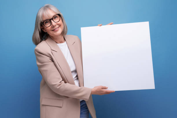 istock cute old woman in a jacket with a mocap poster on a bright background with copy space 1672870928