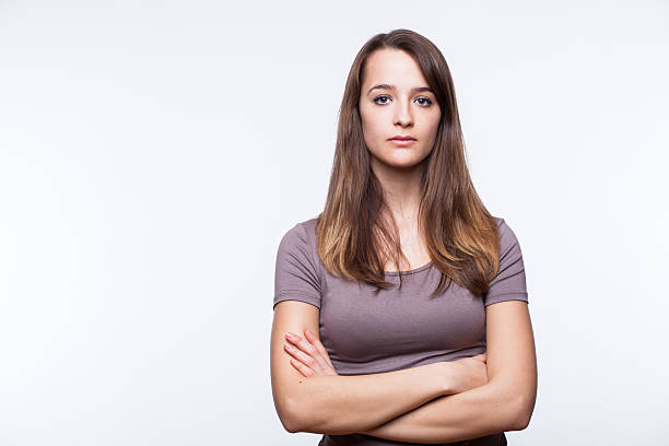 Serious Young Woman With Arms Crossed Portrait of a young woman on a white background. grave stock pictures, royalty-free photos & images