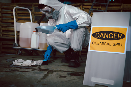 Manual worker in protective work wear spraying virus and bacteria disinfection in underground garage of residential building with sprayer.