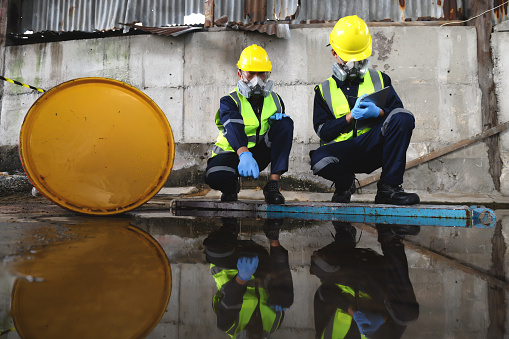 Two Officers of Environmental Engineering Wearing Protective Equipment with Gas Masks Inspected Oil Spill Contamination in Warehouse Old, Hazardous Fuel Leakage and Environmental Concept.