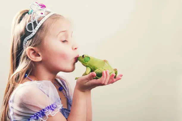 a little girl princess kissing a frog with copy space.