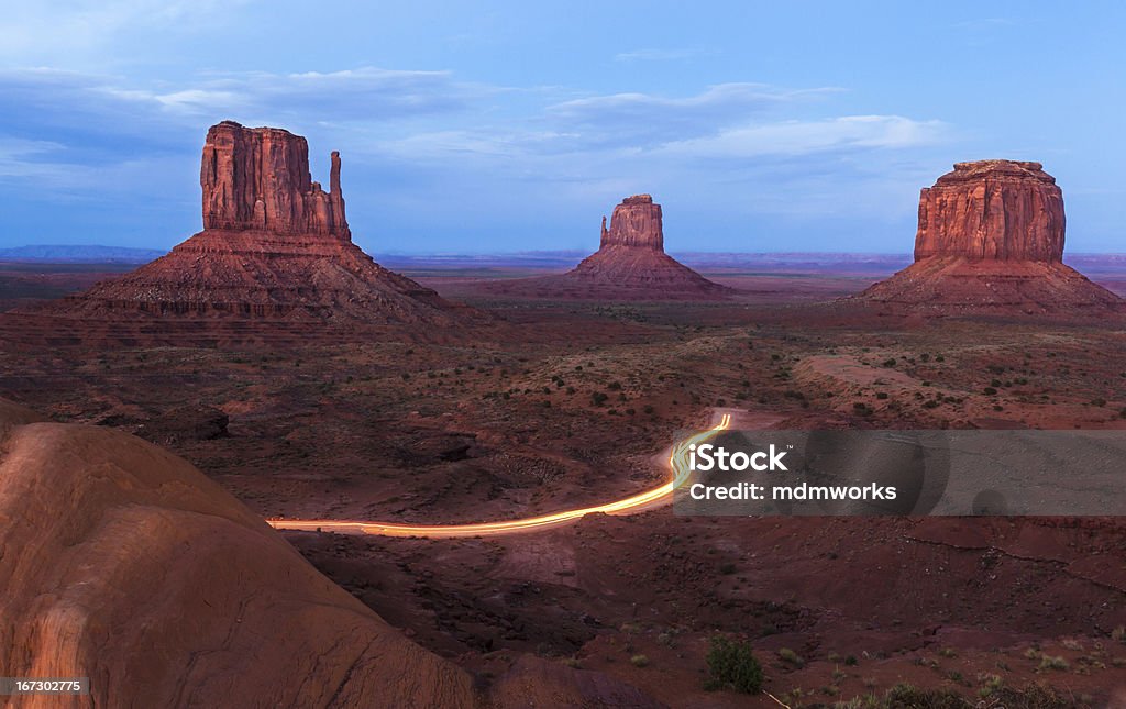 Monument Valley The Mittens and Merrick Butte after sunset with tourists cars coming back from the scenic driver, a 17 mile unpaved loop road that winds through the park. Monument Valley Navajo Tribal Park. Butte - Rocky Outcrop Stock Photo