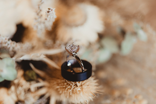 Wedding ring and black wedding band with flowers in background