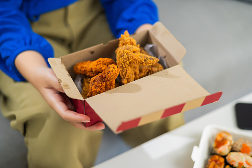 Close up hands of young woman holding a box of chicken fried, She Indulging in Crispy Chicken at home, junk food delivery concept