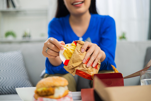 Close up shot of tasty meaty hamburger with vegetables in hands of Black man standing at light blue background